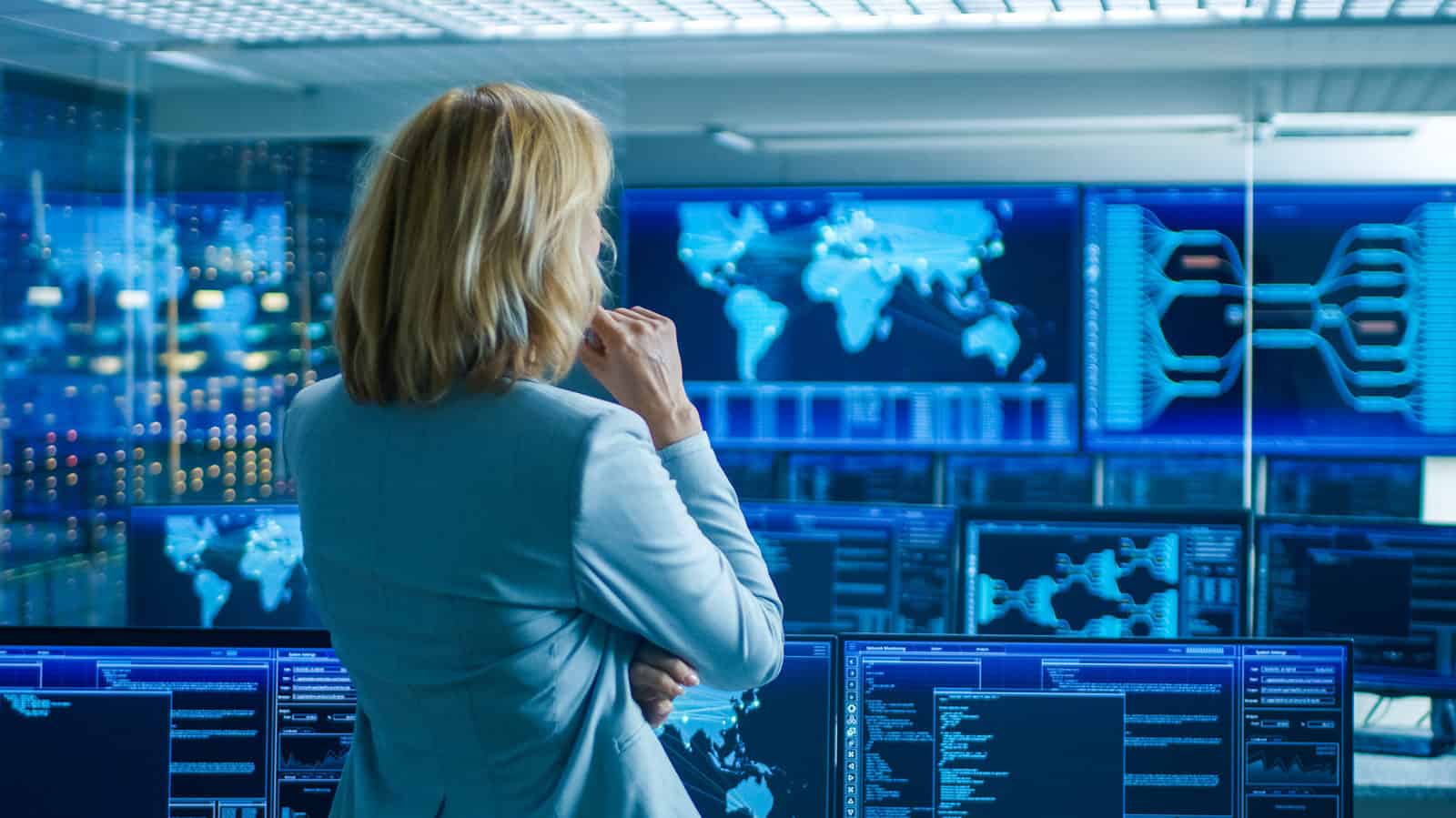 woman standing in a security control room looking at screens with data